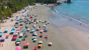 A beach with rows of umbrellas and beach chairs, a sandy shore, and a calm sea. - COSTA LINDA ART HOSTEL  (Quepos)