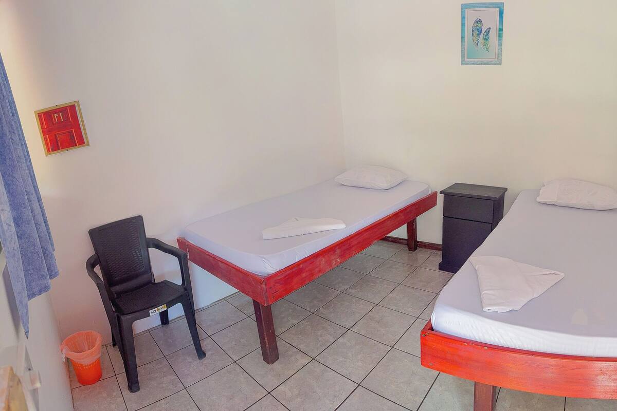 A room with two single beds, a chair, a small table, and a red door.