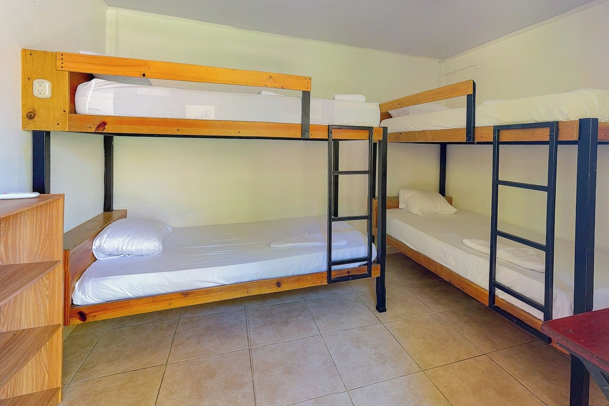 A dormitory room with bunk beds, a wooden desk, and a tiled floor.