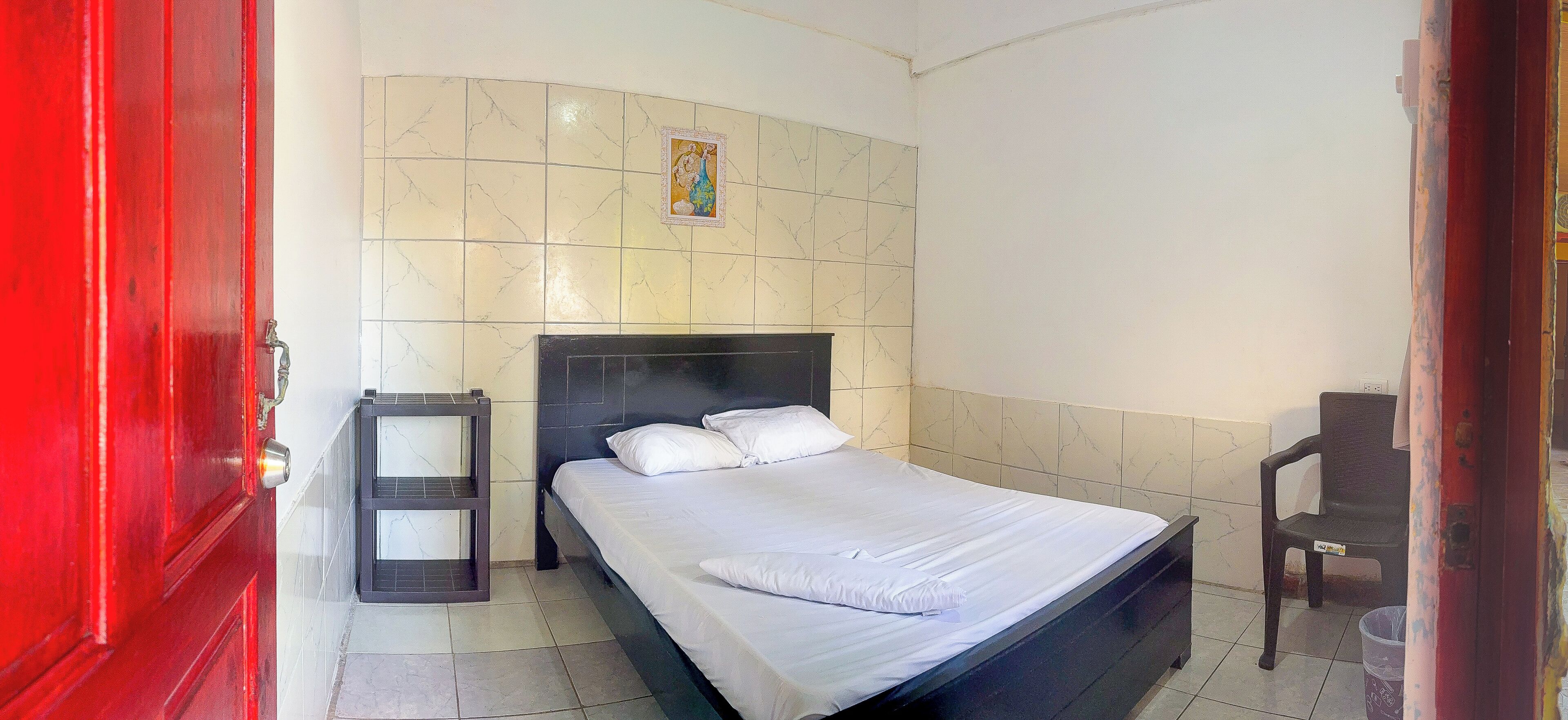 Un dormitorio con cama, mesita de noche, una silla y un cuadro colgado en la pared.