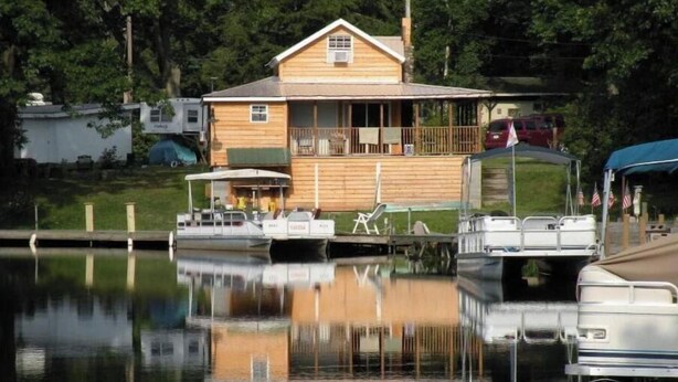 Ein Holzhäuschen mit Balkon, anlegende Boote und einem ruhigen See.