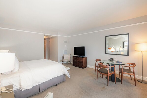 A hotel room with a bed, a desk with two chairs, a television, and a lamp. - Elegant King Studio Suite + Kitchenette (Miami)