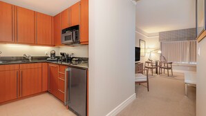 A compact kitchen with wooden cabinets, a stainless steel refrigerator, and a microwave. - Elegant King Studio Suite + Kitchenette (Miami)