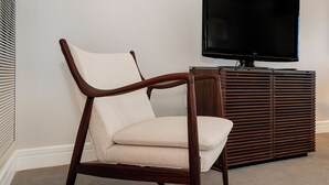 A wooden chair with a cushioned seat and backrest, positioned in front of a dark wooden cabinet and a flat-screen TV mounted on the wall. - Elegant King Studio Suite + Kitchenette (Miami)