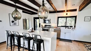 Una cucina moderna con mobili bianchi, una grande isola con sgabelli da bar e un soffitto in legno.