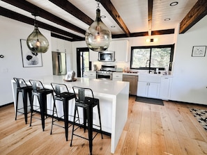 A modern kitchen with white cabinets, a large island with bar stools, and a wooden ceiling.