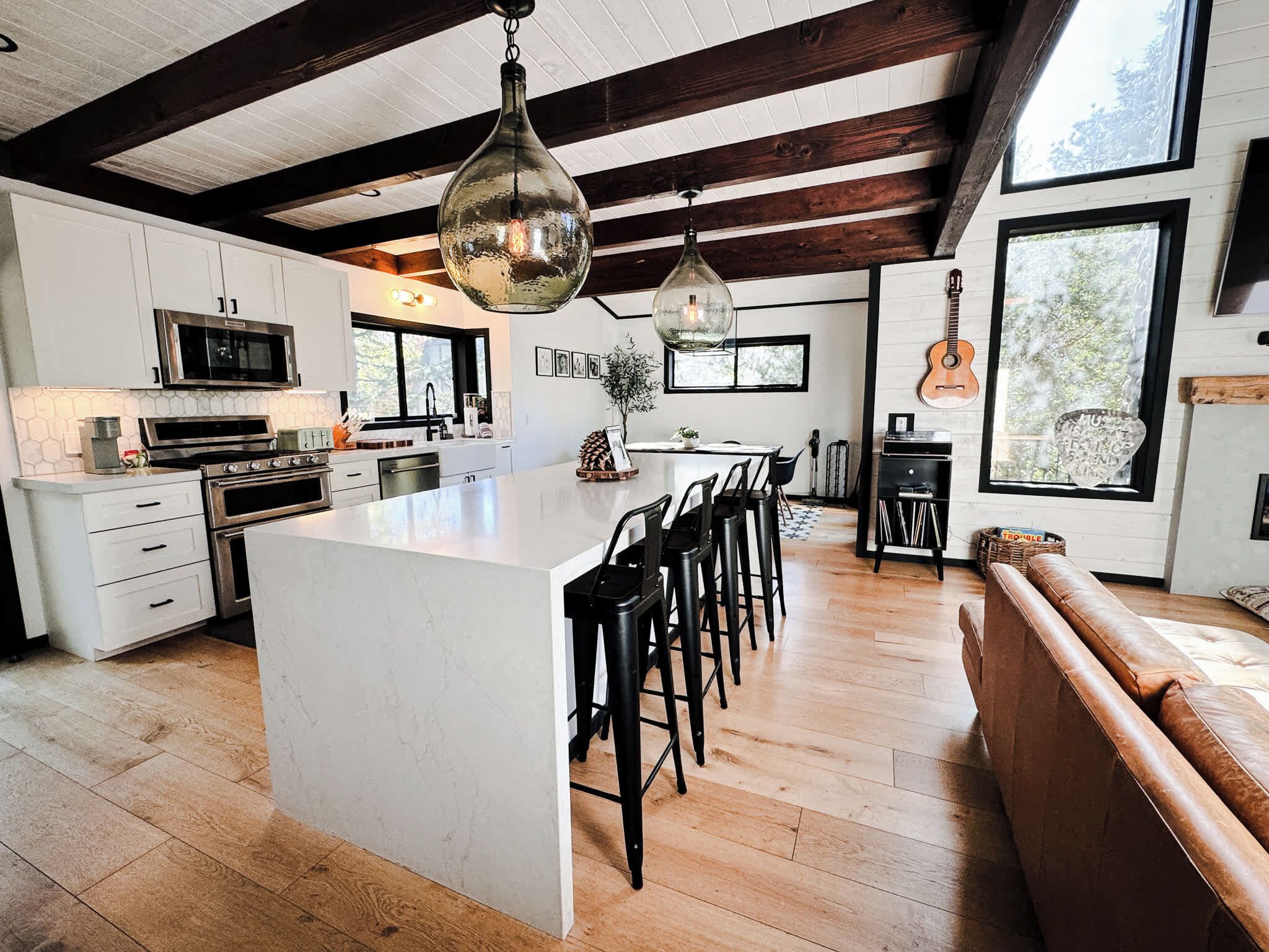 A modern kitchen with a large island, wooden beams, and a guitar wall.