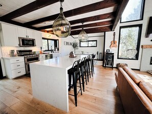 A modern kitchen with a large island, wooden beams, and a guitar wall.