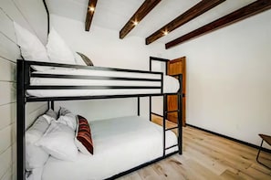 Ein Stockbett mit weißer Bettwäsche, Holzbalken an der Decke und einer Holztür.