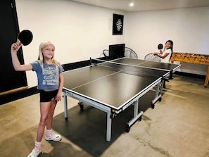 Uma mesa de pingue-pongue numa sala com um alvo de dardos e uma mesa de futebol de mesa.