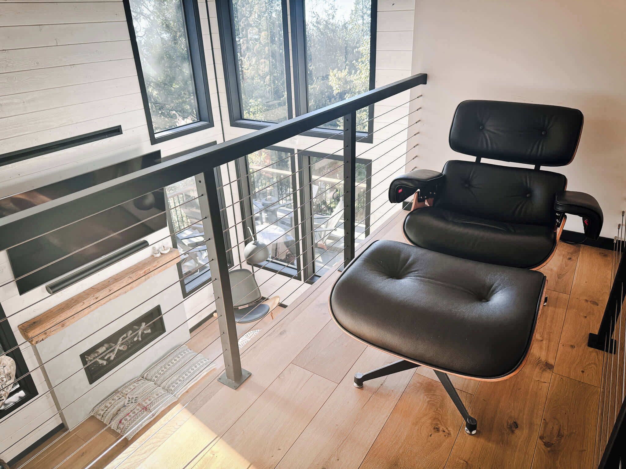 A modern room with a black leather chair, a glass railing, and a view of the outdoors.