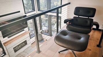 A modern room with a black leather chair, a glass railing, and a view of the outdoors.