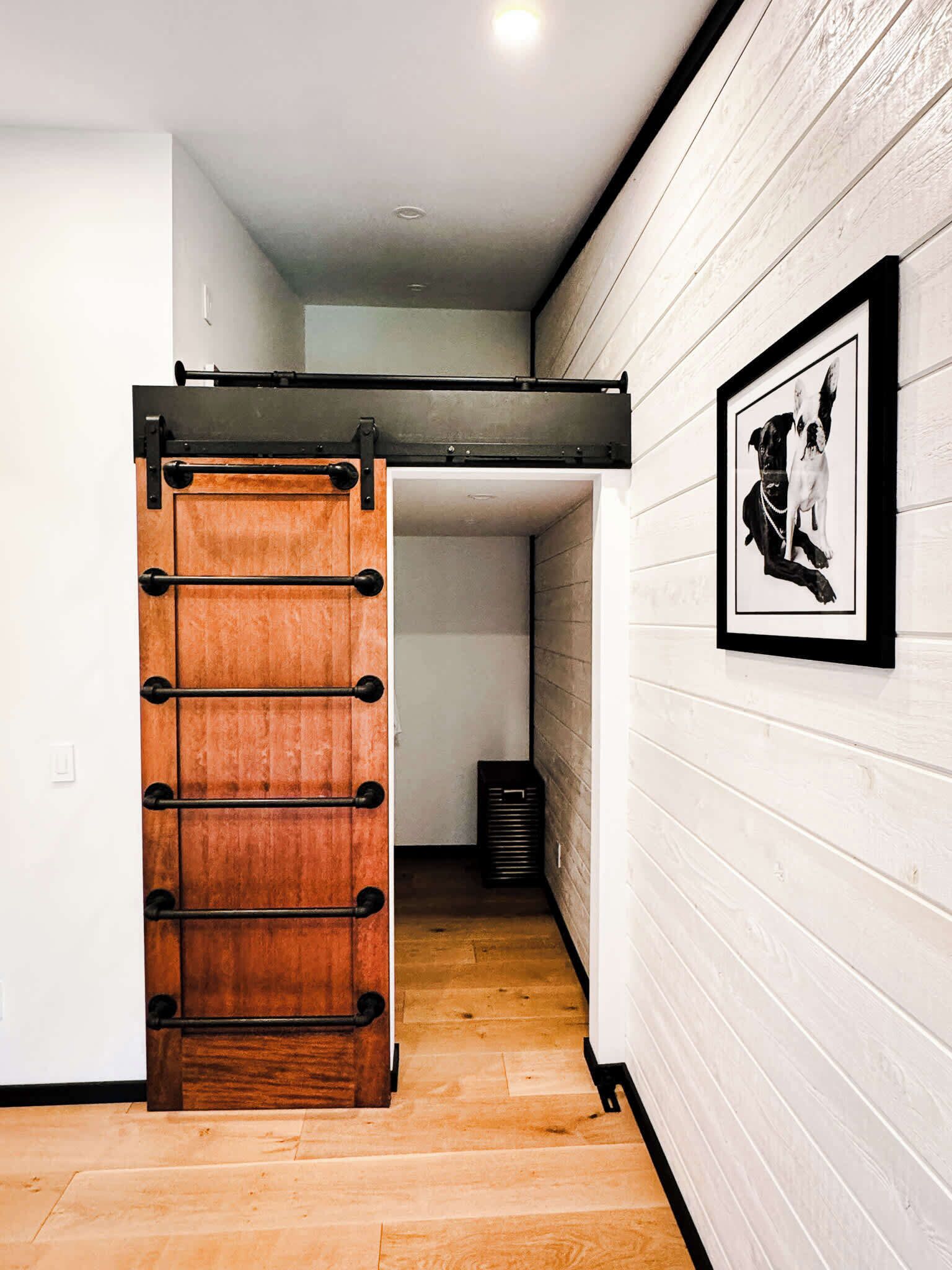 Quarto com piso de madeira, porta deslizante e quadro na parede.