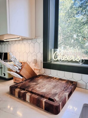 Eine Küche mit einem Holztisch, einem Toaster und einem leuchtenden Schild mit der Aufschrift 'Cheers'.