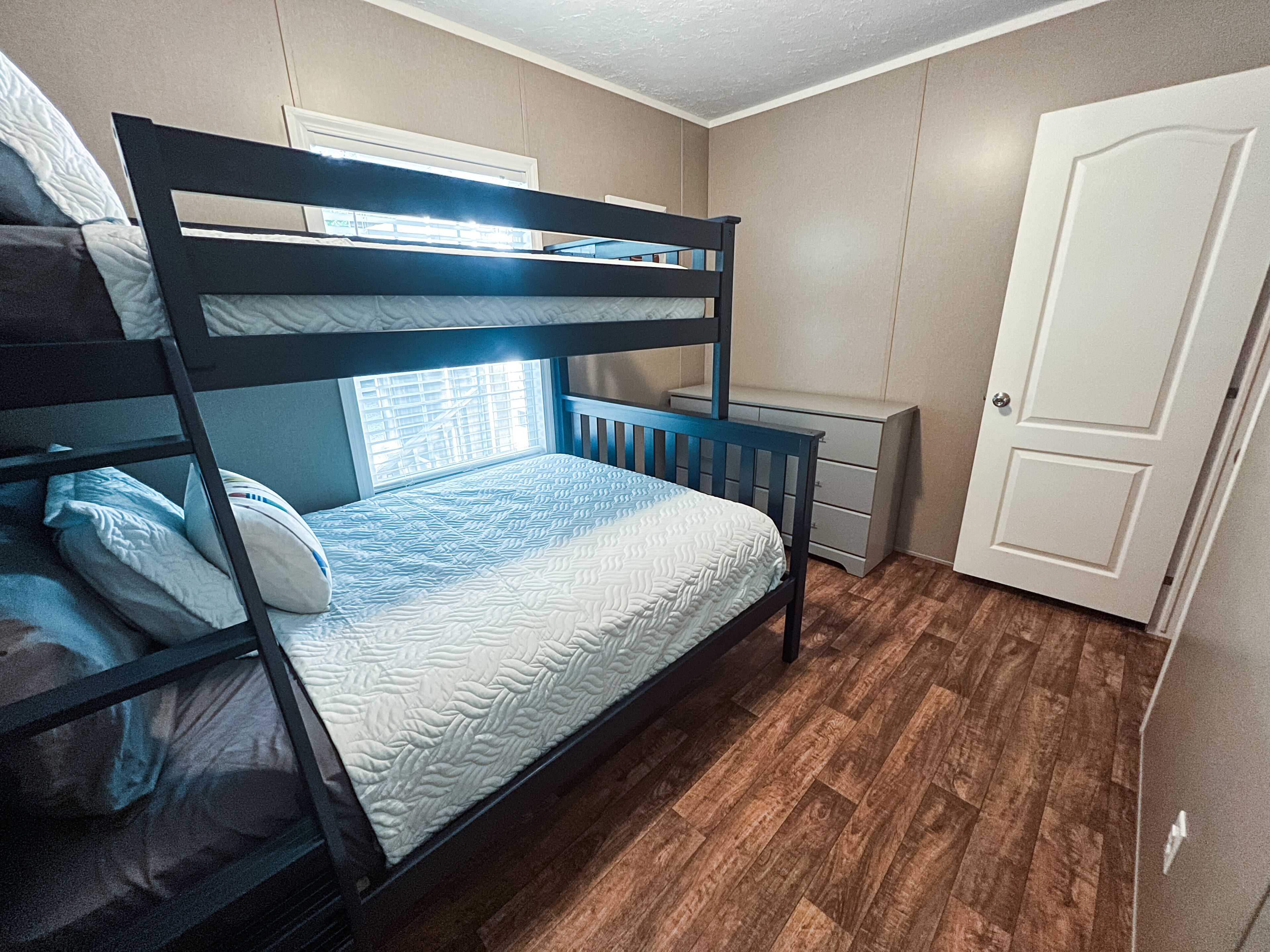 A bunk bed room with a window, a desk, and a door.
