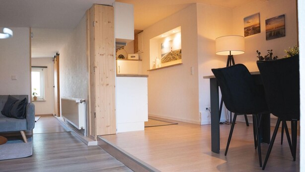 A modern living space with a wooden floor, a dining area with black chairs, a kitchen with a wooden cabinet, and a painting on the wall. - Großes Meer (Südbrookmerland)