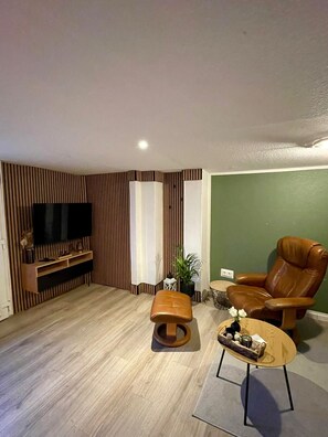 A modern living room with a flat-screen TV, leather armchair, ottoman, and a coffee table. - Großes Meer (Südbrookmerland)
