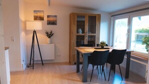 A dining area with a wooden table, black chairs, a lamp, and a cabinet with glass doors. - Großes Meer (Südbrookmerland)