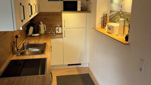 A compact kitchen with white cabinets, a microwave, a sink, and a small refrigerator. - Großes Meer (Südbrookmerland)