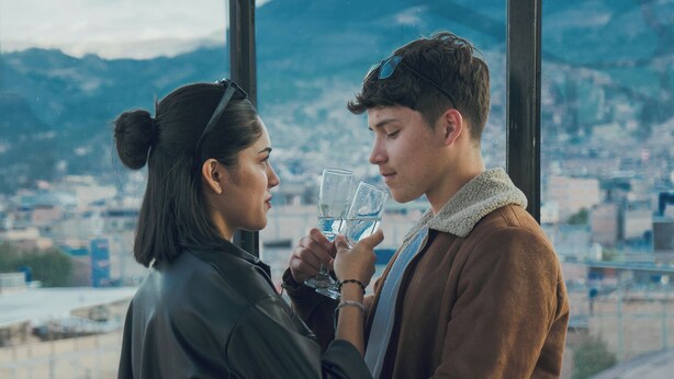 Una pareja de pie junto a una ventana con vistas a un paisaje urbano y montañas.