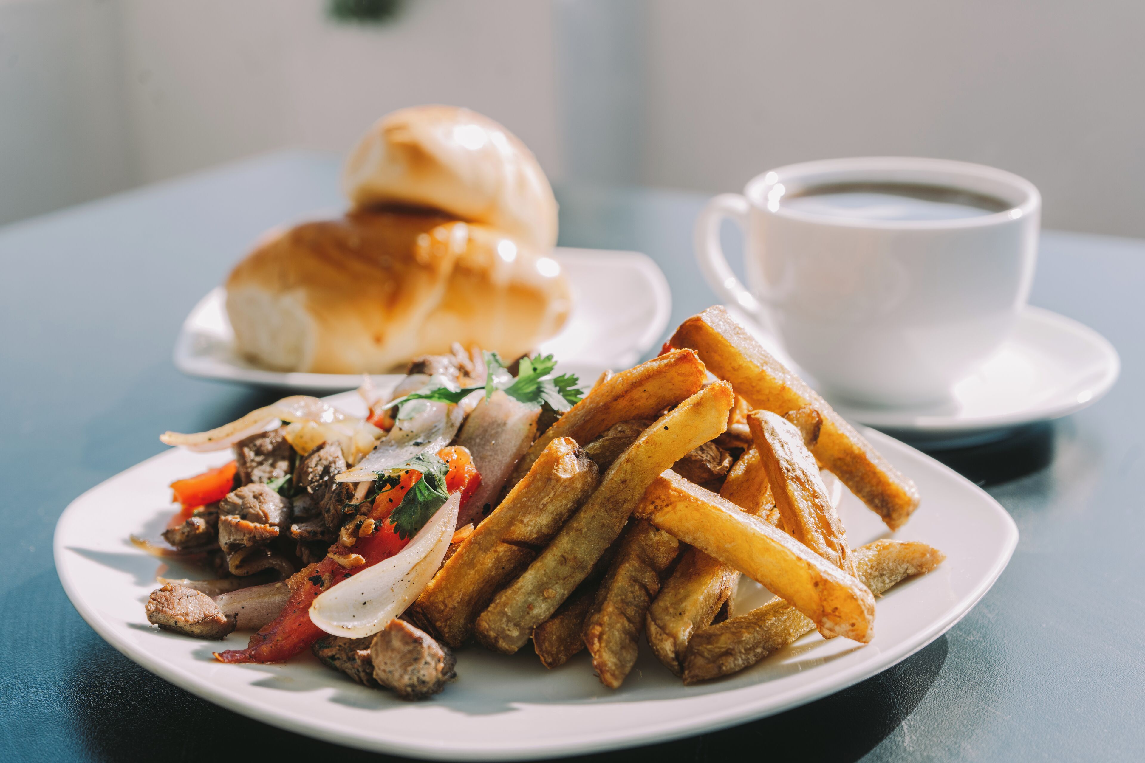 Un plato de comida con papas fritas, carne y verduras, además de una taza de café sobre una mesa.