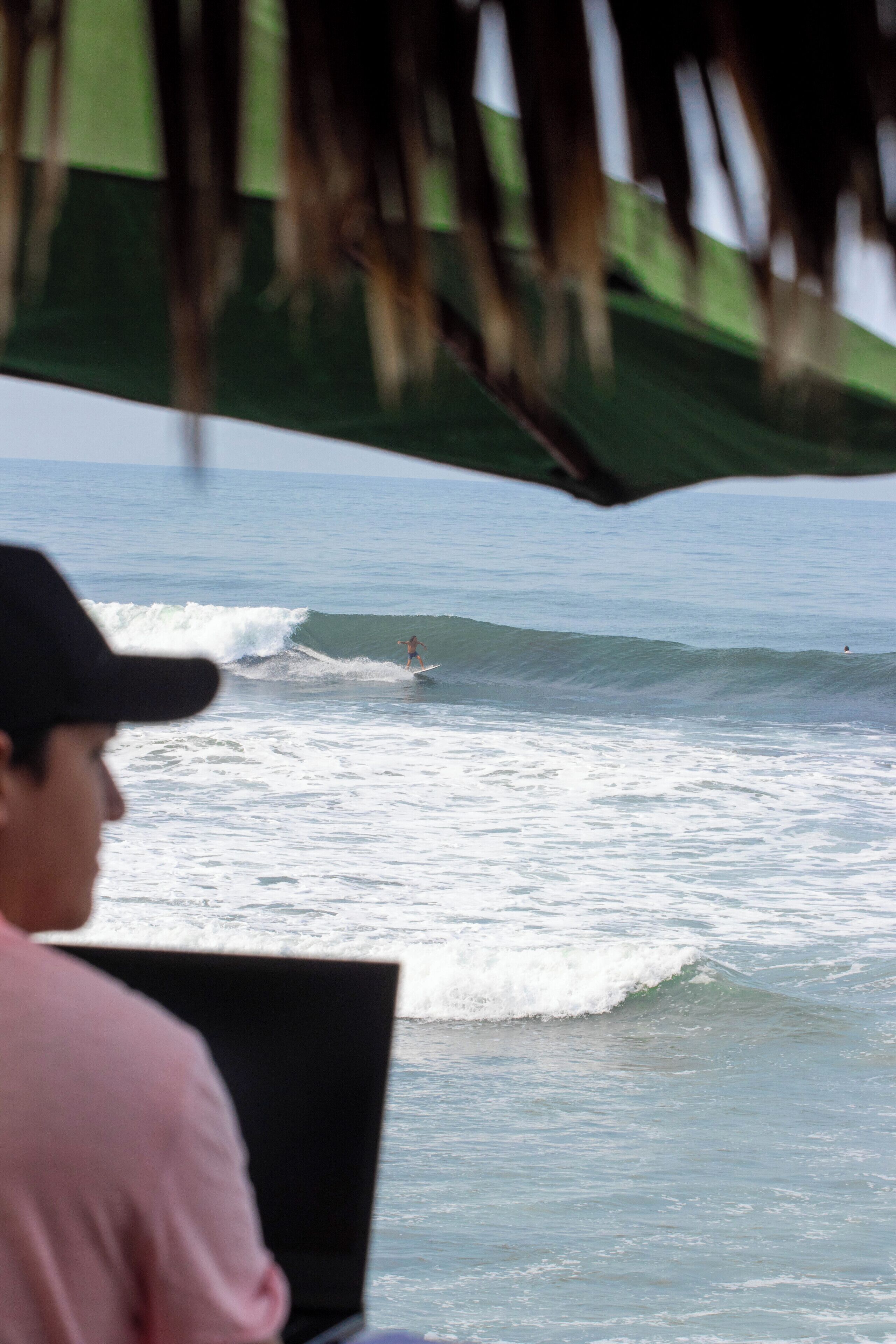 A person sitting at a table with a laptop, overlooking the ocean with waves.