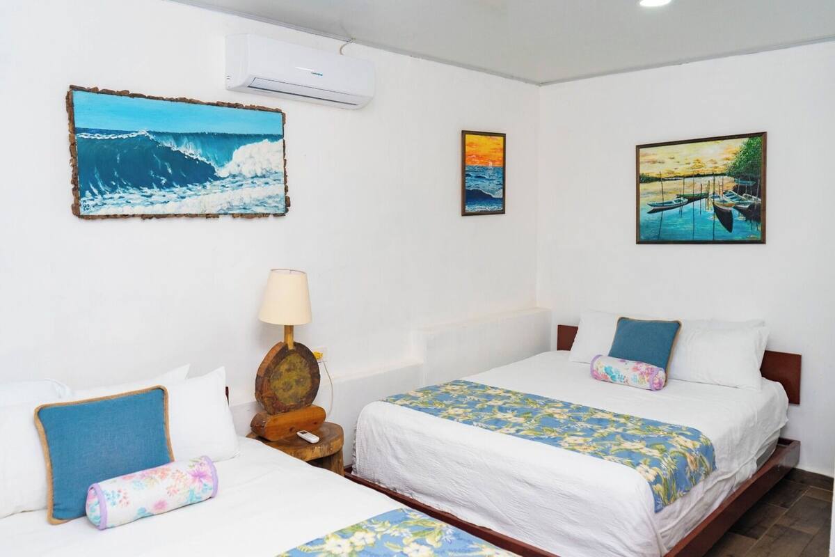 A hotel room with two beds, a nightstand, a lamp, and three paintings on the walls.