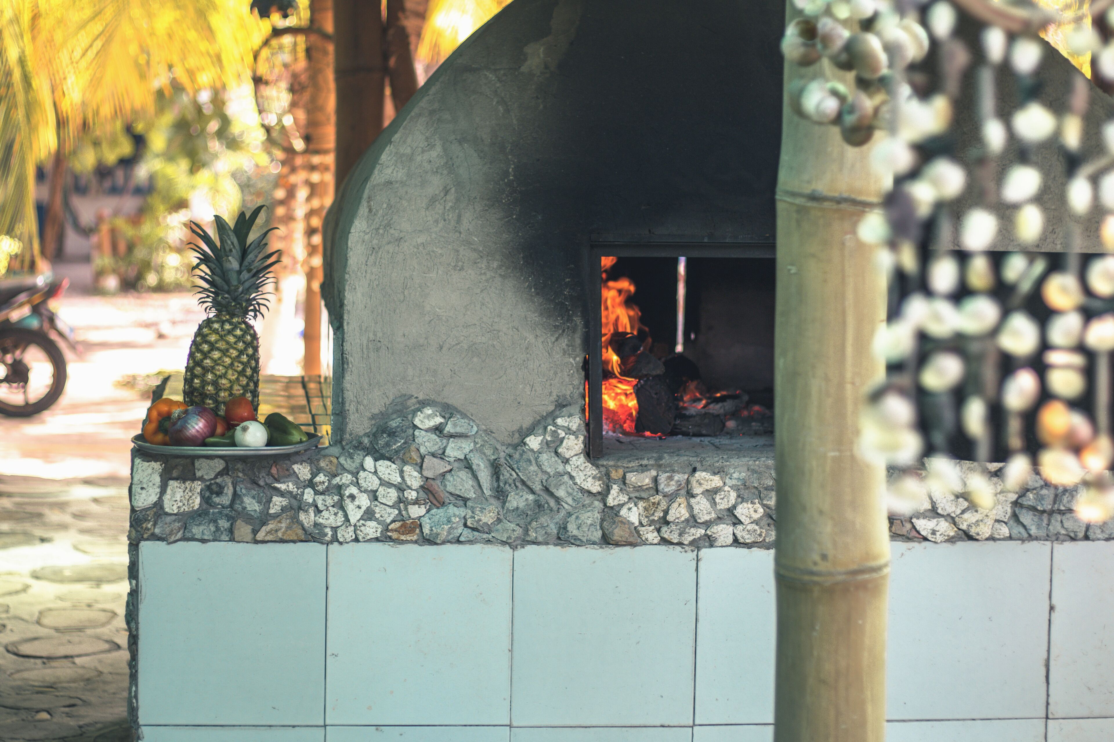 Una cocina al aire libre con piso de piedra, una chimenea rodeada por una valla de bambú y un muro de azulejos.