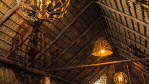 Un intérieur doté d’un toit de chaume, de meubles en bois et de luminaires sphériques suspendus.
