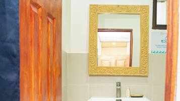 A bathroom with a wooden door, a white sink, a mirror with a decorative frame, and a shelf with folded towels.