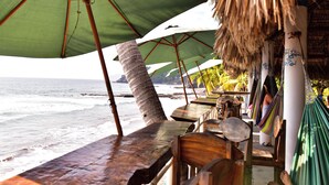 Un restaurant situé en bord de mer, avec des tables en bois et des parasols verts, offrant une vue sur l’océan.