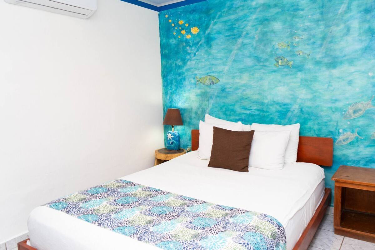 A bedroom with a bed, a nightstand, a lamp, and a wall with a blue mural.