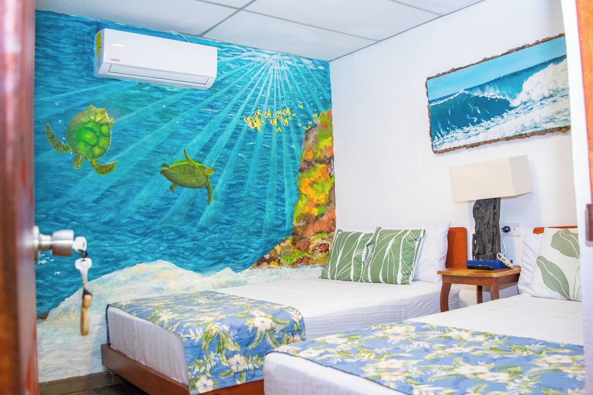 A room with two beds, a mural of ocean waves, and a painting of a wave.