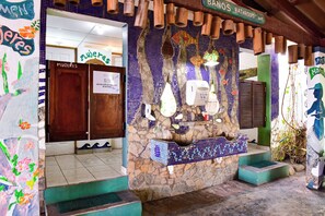 A bathroom with a mosaic wall, a wooden door labeled "MUJERES", and a sign above the door reading "BAHOS BATHROOM WC".