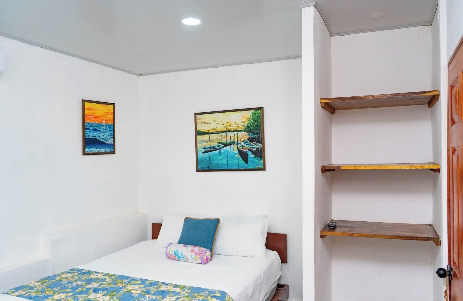 Une chambre à coucher avec un lit, deux tableaux, une étagère en bois et une porte.
