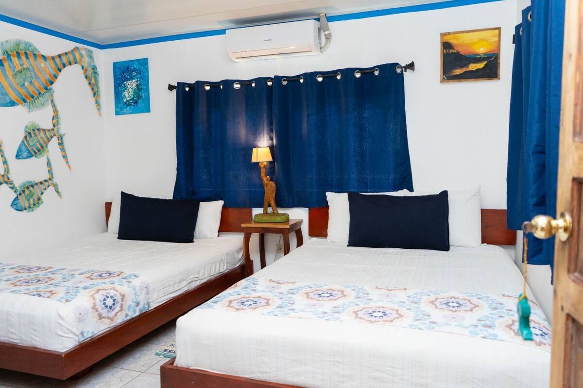 A hotel room with two beds, a nightstand, a lamp, a painting, and a window with curtains.