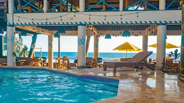 Une piscine intérieure dotée de chaises longues et de parasols, entourée de piliers et offrant une vue sur l’océan.