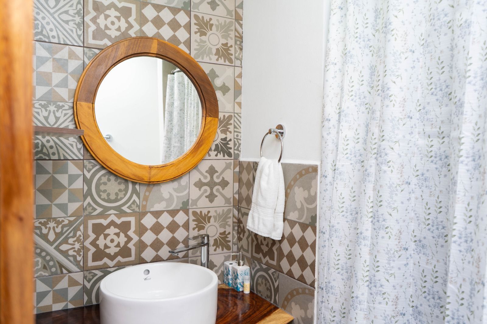 A bathroom with a round mirror, a sink, patterned tiles, a towel rack, and a shower curtain.