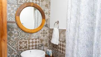 A bathroom with a round mirror, a sink, patterned tiles, a towel rack, and a shower curtain.