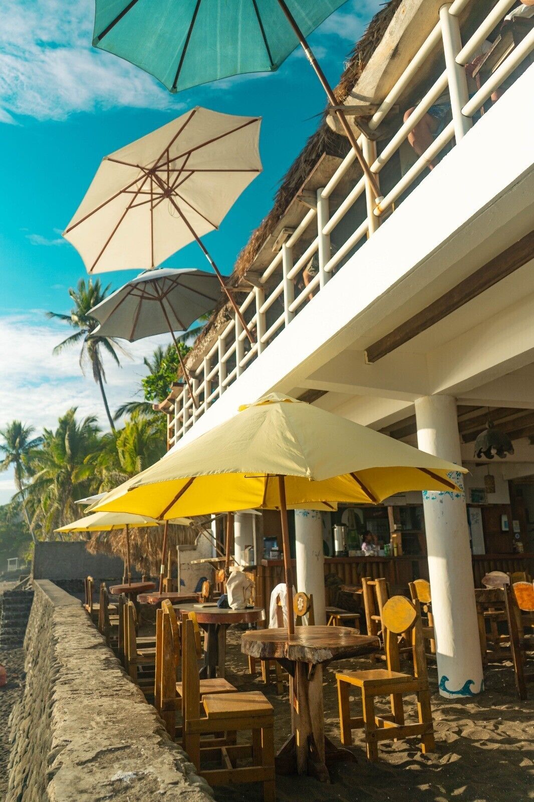 A beachfront restaurant with outdoor seating, umbrellas, and a view of the ocean.