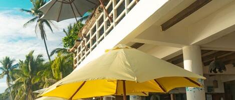 A beachfront restaurant with outdoor seating, umbrellas, and a view of the ocean.