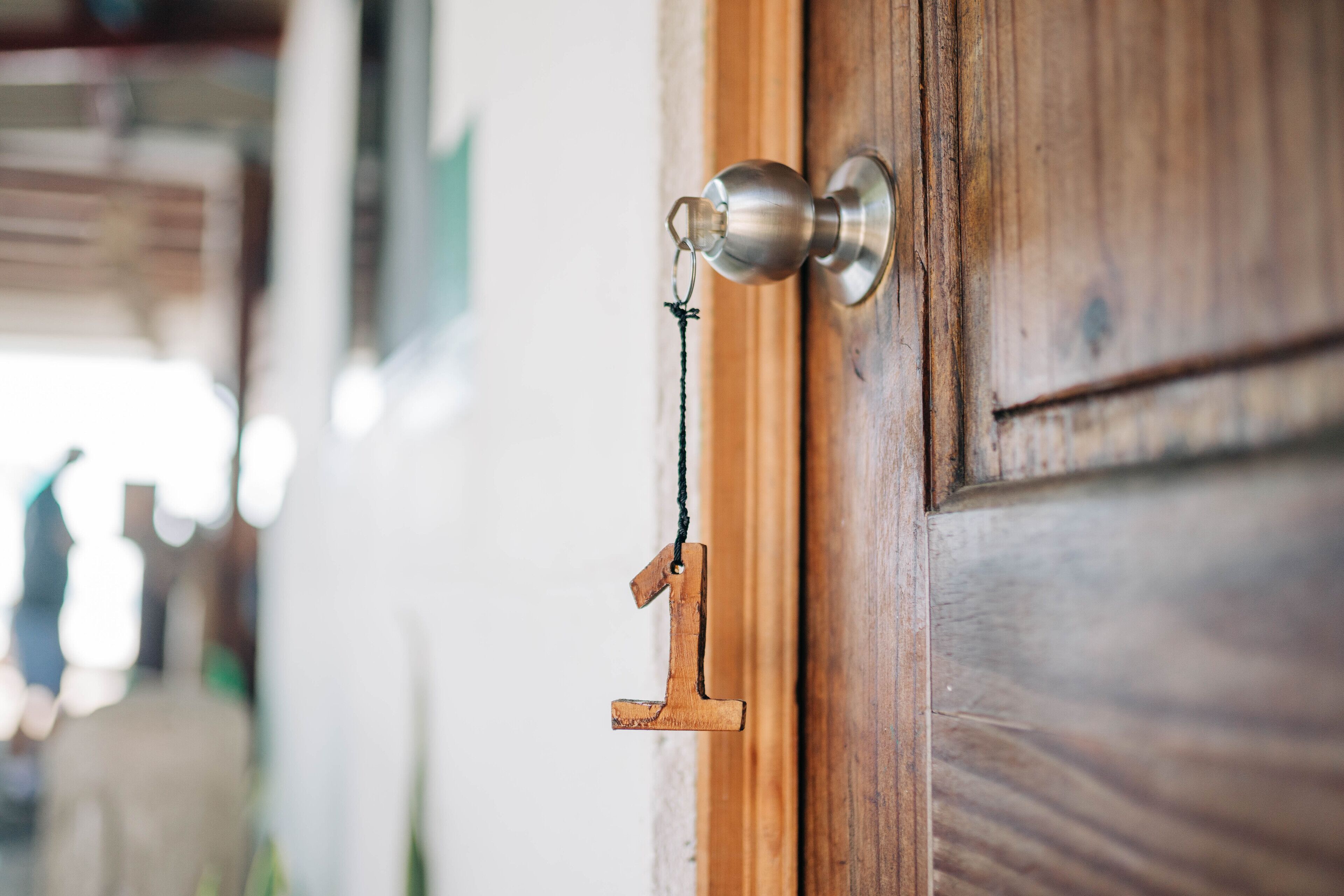 Une porte en bois avec une poignée de porte en métal et un porte-clés orné d’un pendentif en bois en forme de chiffre « 1 ».