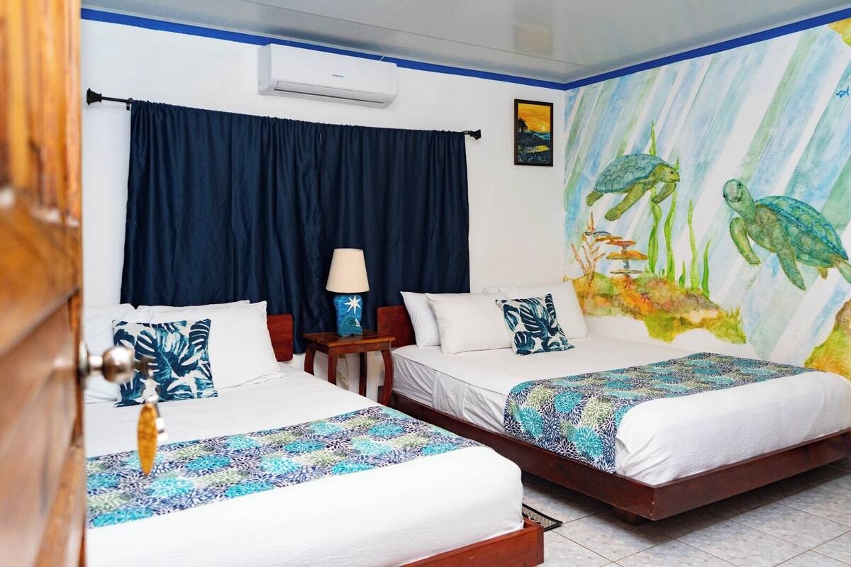 A hotel room with two beds, a nightstand, a lamp, and a mural of sea creatures.