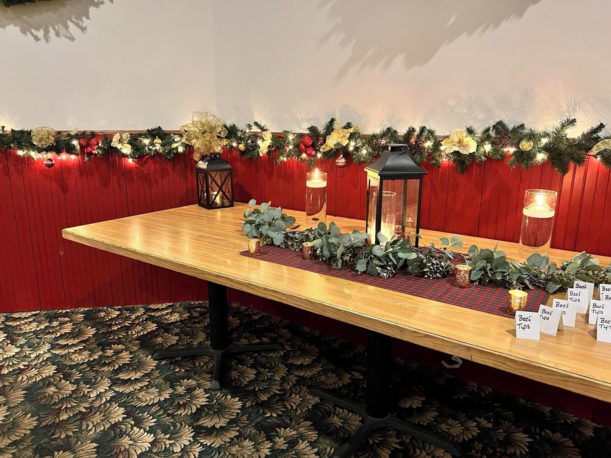 A wooden table with a red plaid runner, decorated with greenery and candles, against a red wall with a garland.