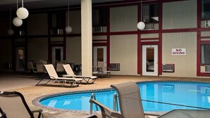 Une piscine intérieure dotée de chaises longues et d’une table, le tout sous un haut plafond percé d’une verrière.