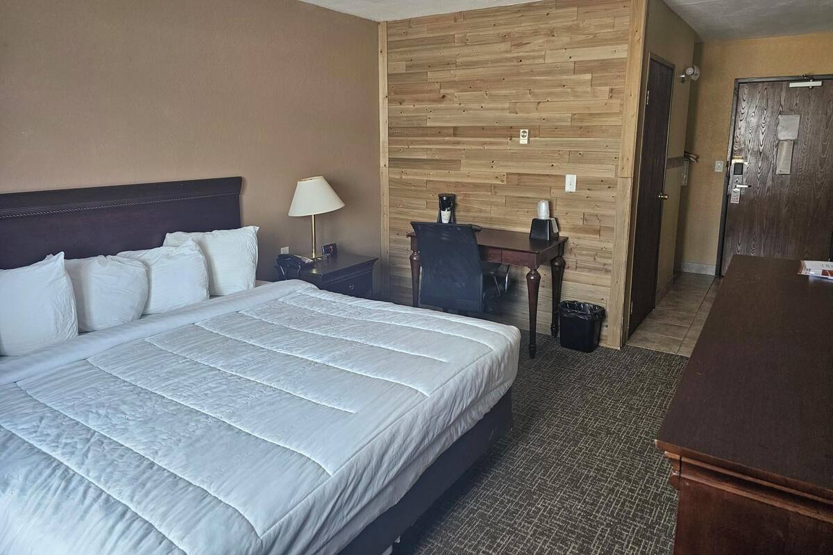 Hotellihuone, jossa on suuri sänky, työpöytä, tuoli, lamppu ja roskakori.