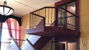 Un intérieur moderne avec un escalier menant à un deuxième étage, un grand lustre et un panneau d’avertissement au sol.