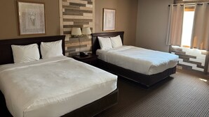 Une chambre d’hôtel avec deux lits, une tête de lit en bois, une table de chevet avec des lampes et des œuvres d’art encadrées accrochées aux murs.