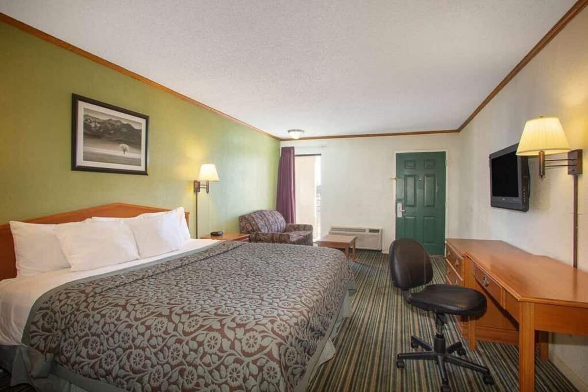 Habitación de hotel con cama, escritorio, silla, televisor y un cuadro en la pared.