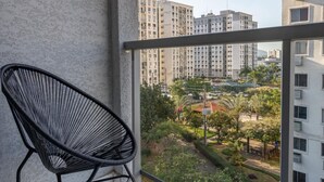 A balcony with a black chair, a tiled floor, and a view of high-rise buildings and greenery. - Charm in Barra da Tijuca Great Wifi Sa508 (Rio de Janeiro)